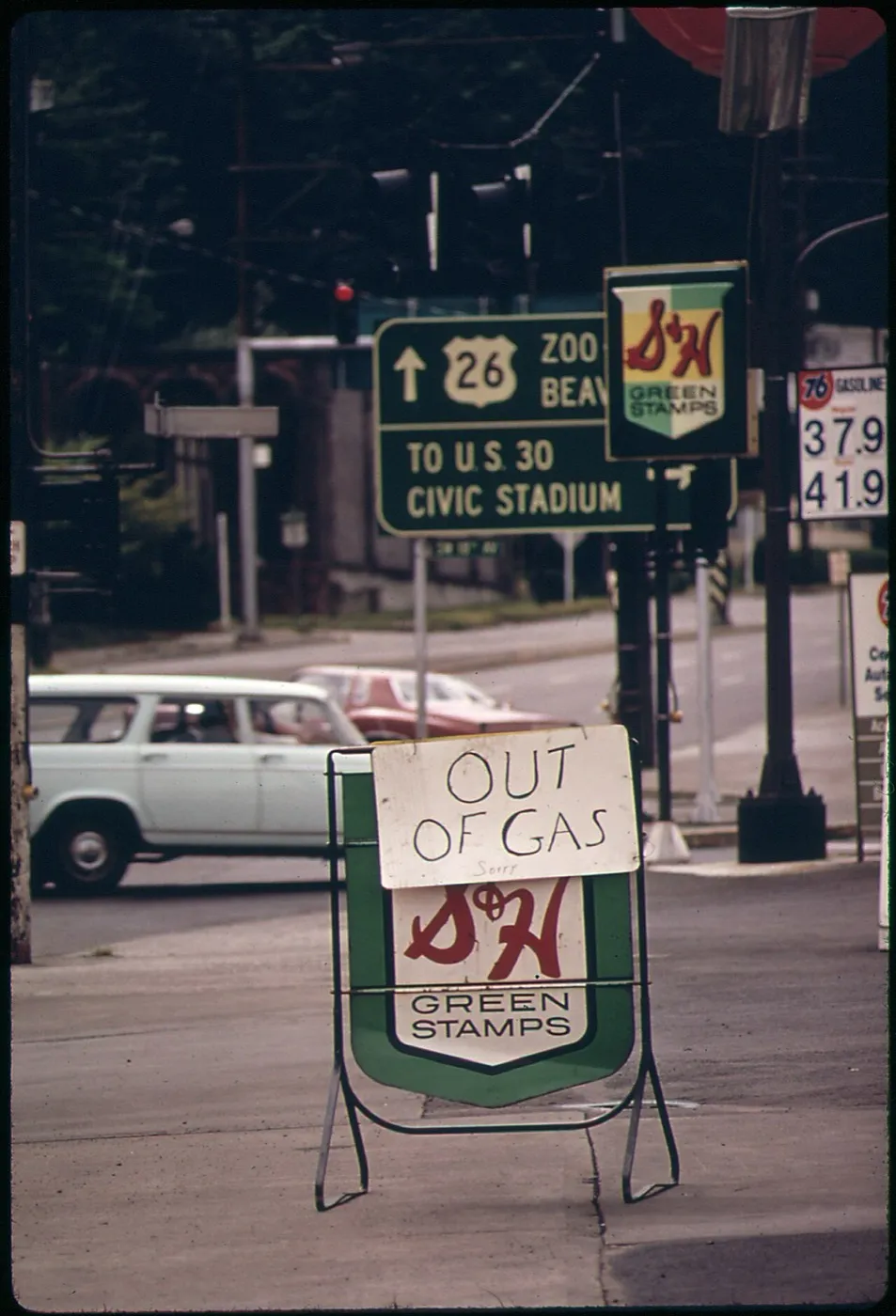 A sidewalk sign with the S&H Green Stamps emblem and a hand-lettered card reading “Out of gas,” at a Portland, Ore., corner in 1973