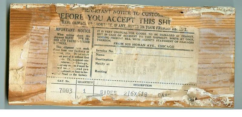 A torn paper shipping label glued to a board, printed “Before you accept this shipment” and “From 925 Homan Ave., Chicago,” with a line for catalog number 7883