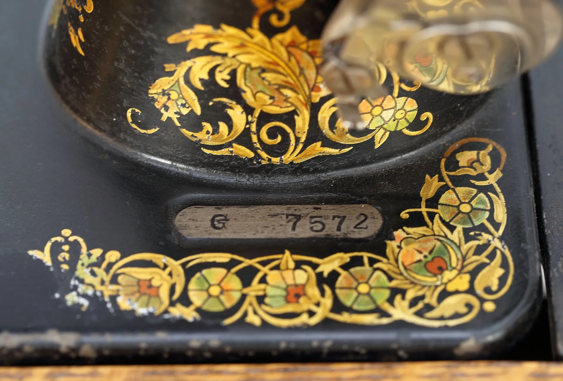 A small metal plate stamped G 7572 set into the black bed of an old Singer, surrounded by gold and colored floral decals