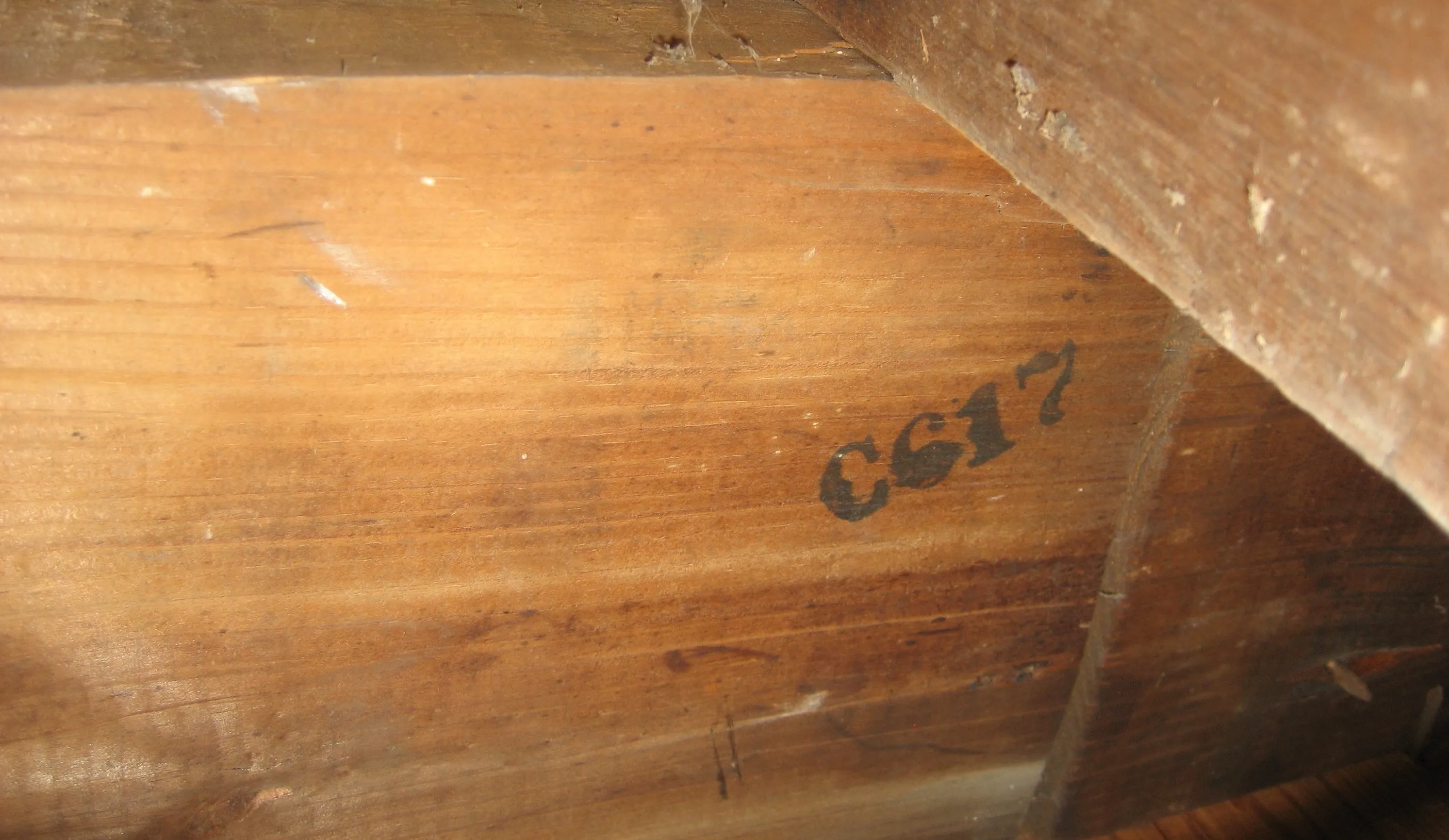 A wooden framing board with the black stamp C617 on its side, under a dusty crossing beam