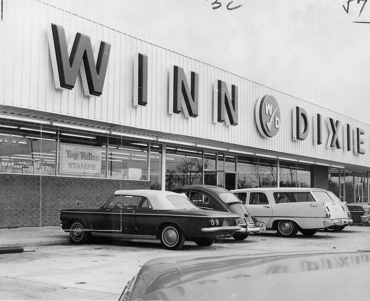 Black-and-white photo of a new Winn-Dixie supermarket with big block letters across the front, a Top Value Stamps sign in the window and early-1960s cars parked outside
